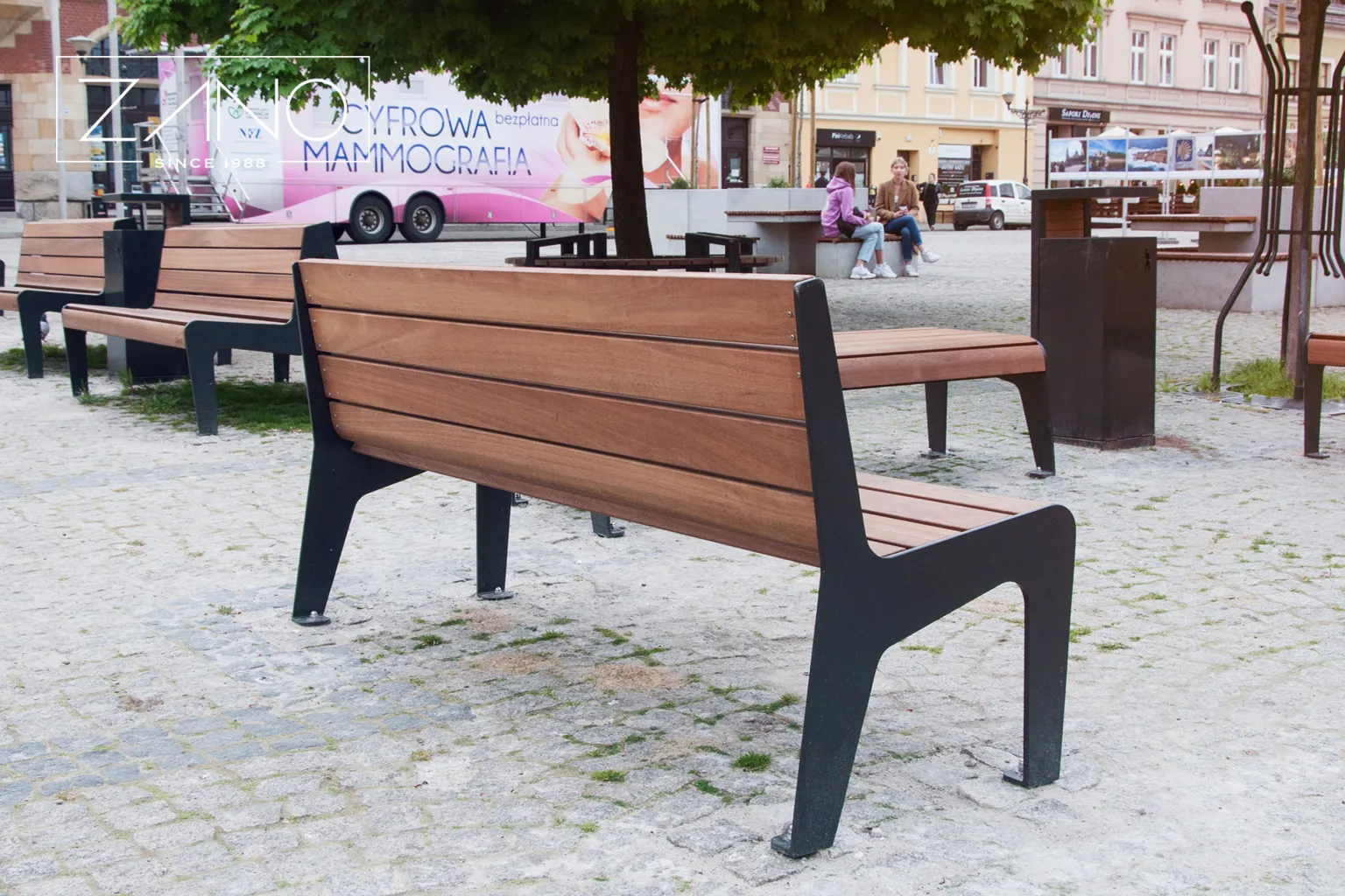 En modern stadsbänk med ryggstöd, träsits och robusta svarta stålstöd på sidorna.