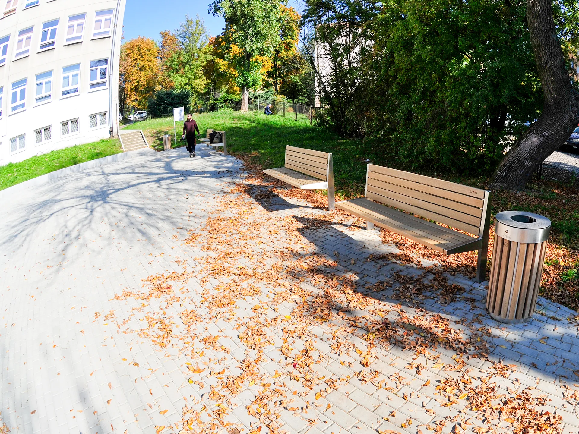 En modern stadsbänk med sitt- och ryggstöd i trä på en rak stålram samt en rund papperskorg